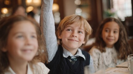 Fototapeta premium Three young children, two girls and a boy, sitting at a table in a restaurant. the boy is in the center of the image, with his arm raised in the air and a big smile on his face.