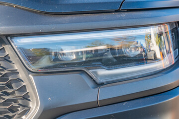 Close-up view of dark gray SUV front grille, grid patterned grille, headlights, fog lights, daytime outdoor lighting, angled side perspective