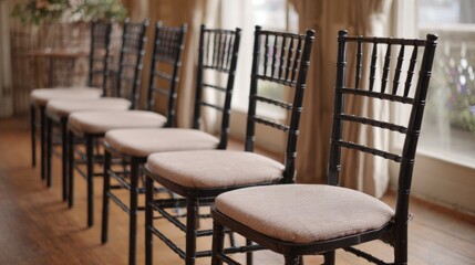 Fototapeta premium Row of six black wooden chairs with beige cushioned seats. the chairs are arranged in a line and are facing towards the right side of the image.