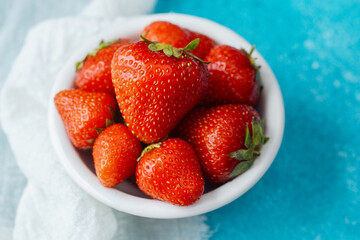 bowl of fresh whole strawberries close up on blue background