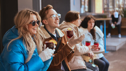 Group of young friends laughing and drinking hot beverages outdoors. Concept of social connection, cafe promotion, and urban joy for lifestyle, event, and brand visuals.