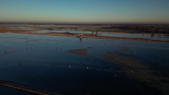 Aerial view of a windmill amidst waterways reflecting the sky, contrasting with the dark shadows and land textures, Ryptsjerk, Friesland, Netherlands.