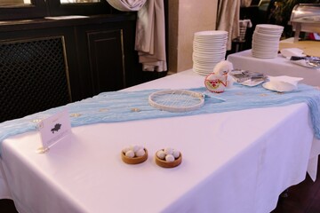 White buffet table with light blue sheer runner, decorative dream catcher, small sheep toy, and bowls of white round sweets