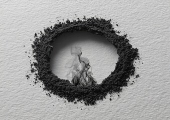 Circular boundary of dark powder on textured surface with abstract black smoke emerging from its core, symbolizing transition or decay