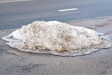 Thawing snow residue near curb showing dirty slush after city snow removal and maintenance operation, municipal snow clearing aftermath leaving dirty icy pile along street edge with thawing runoff