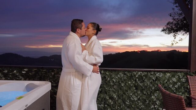 Romantic couple in bathrobes kissing at sunset on a terrace with a jacuzzi