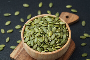 Pumpkin seeds in wooden bowl on cutting board with black background