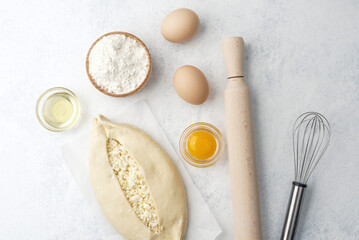Raw khachapuri with egg yolk and cheese on white background with ingredients