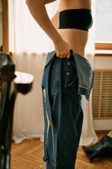 Young woman in lingerie putting on jeans. She has a beautiful slim figure and looks natural and confident. Soft light emphasizes her femininity and elegance, creating an aesthetic and intimate atmosph