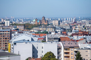 Panoramic view of Belgrade, Serbia, capturing the city’s blend of historic and modern architecture under a clear blue sky, with the striking red-brick Church of Saint Mark .