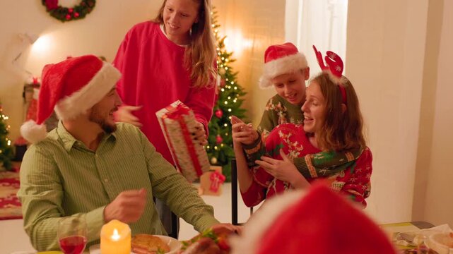 Boy and girl making surprise and giving present or gift box to their mom and dad on Christmas Day