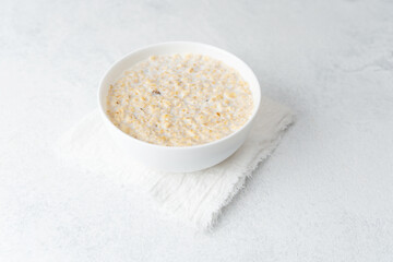 Bowl of creamy oatmeal porridge on white towel background