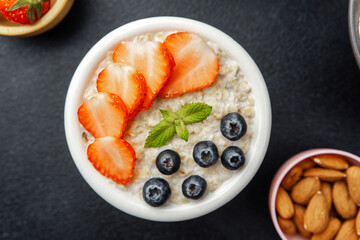 Oatmeal with strawberry blueberry and mint in white bowl on black background