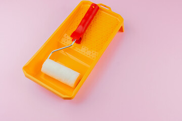 Red handled roller in yellow tray on pink background for home painting and renovation concept