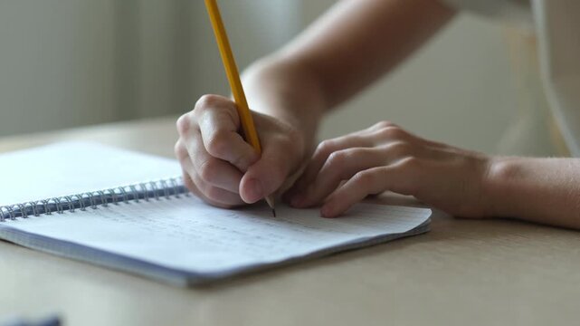 Close up hand of kid girl writing, school child doing homework sitting at table. Student studying indoors. Education concept. Selective focus