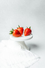 Fresh strawberries displayed on a white cake stand in a minimalist setting
