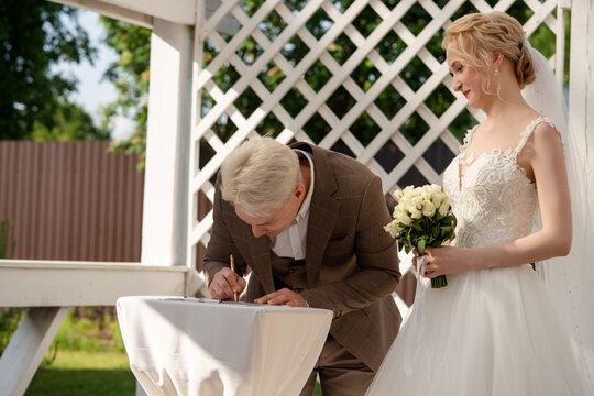 Couple signing marriage certificate under garden gazebo at outdoor wedding