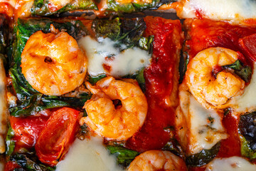 Pizza with shrimp, tomatoes and spinach, close-up. Mediterranean pizza texture background