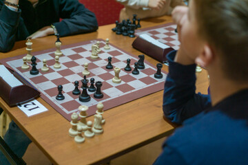 two boys playing chess at a table in an indoor setting, focusing on the chessboard and pieces, concept of strategy game, mental challenge, competition, education, hobby, indoor activity