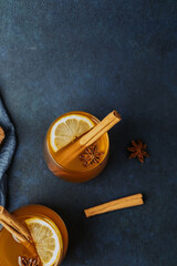 Warm spiced beverage with lemon slices, cinnamon sticks, and star anise on dark surface. © reddish