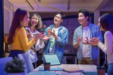 ibrant group of young startup professionals celebrate success during a late-night virtual meeting in a modern office, applauding with happiness and laughter. The confident team of AI-driven strategist