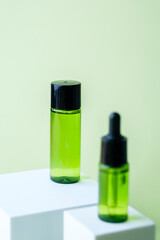 Green cosmetic dropper bottle with black cap displayed with matching container on white cube pedestal background