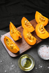 Fresh pumpkin slices on wooden board with oil and salt, prepared for cooking, dark background