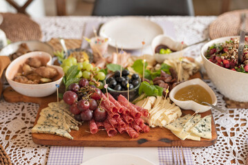 Fresh food for eating on a table for lunch. Cold plate of various salad, cheese, ham, grapes and olives on board. Appetizer for meal in restaurant. Banner.	