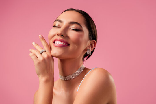 Beautiful young woman with stunning jewelry and glamorous makeup posing against a soft pink background