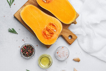 Halved butternut squash on cutting board with herbs, peppercorns, oil, and salt