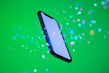 A modern smartphone floats in mid-air against a vibrant green background with colorful bokeh lights.