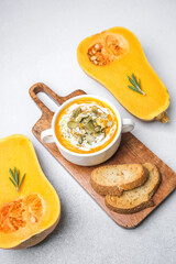 Butternut squash soup bowl with pumpkin seeds and herbs, served with toasted bread slices on wooden board.