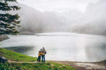 Father and son enjoy a peaceful moment by the serene lake surrounded by mountains on a foggy day