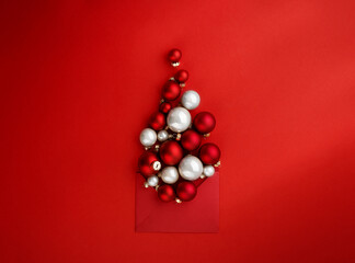 Creative Christmas tree made of Christmas ornaments in shape of balls decorated red ribbon bow on red background. New Year or Christmas greeting card concept. Design element. Top view.