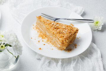 Layered millefeuille cake slice on white plate with fork, pastry cream dessert, delicate pastry