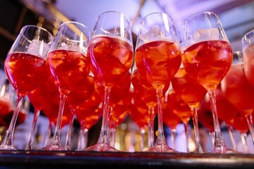 Close-up of a row of bright red spritz cocktails with ice cubes in wine glasses, set against a dark, moody bar background during an event