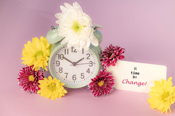 Time for a change message on a tag.  Retro alarm clock surrounded by fresh flowers on a pink background.