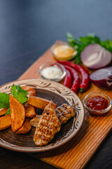 Grilled chicken with potato wedges and sauces on wooden board