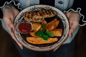 Grilled chicken with potato wedges and salsa held by female hands