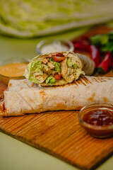 Delicious grilled chicken wrap with fresh vegetables and sauces on a wooden board