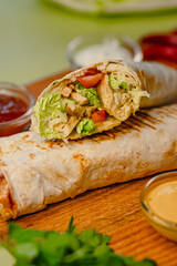 Delicious grilled chicken wrap with lettuce and tomato on a wooden board