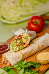 Fresh chicken wrap with vegetables and sauces on wooden board