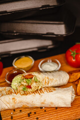 Delicious chicken wrap with fresh vegetables, sauce dips, and wedges on a wooden platter