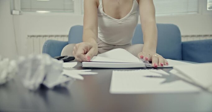 A young woman is seated at a table, tearing pages from a notebook. This video captures the crisp, relaxing sounds of paper ripping, ideal for ASMR content or conveying focused, calming activity.