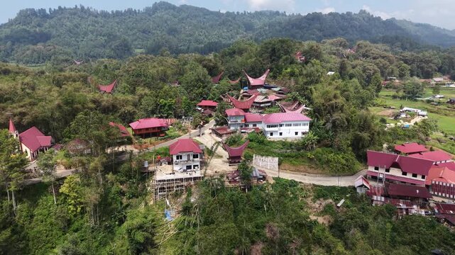 Aerial view of traditional Tongkonan houses with curved roofs on a hillside in Tana Toraja, Indonesia, surrounded by mountains and clouds.	
