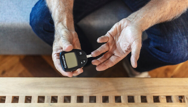 Finger, healthcare and diabetes with a senior man testing his blood sugar level while in his retirement home. Medical, wellness and test with a mature male using a glucometer to measure his glucose.