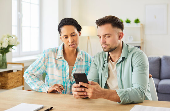 Family couple working together online with phone at home, handling bills and payments, managing debt, collaborating on financial tasks, using internet for joint effort in a domestic space.