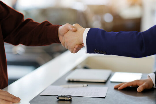 Handshake between professional car salesman in suit and customer after successful business transaction with signed contract, symbolizing customer satisfaction at a dealership