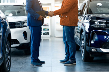 Cropped of two men are standing inside a bright and spacious car showroom. They are shaking hands with each other, appearing satisfied and confident after finalizing a deal on a new vehicle. High