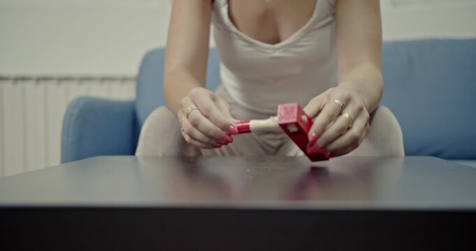 A young woman sits casually on a sofa, demonstrating how to use a classic wooden ratchet noise maker. Hear the distinct, rhythmic sounds as she operates the instrument on a coffee table.